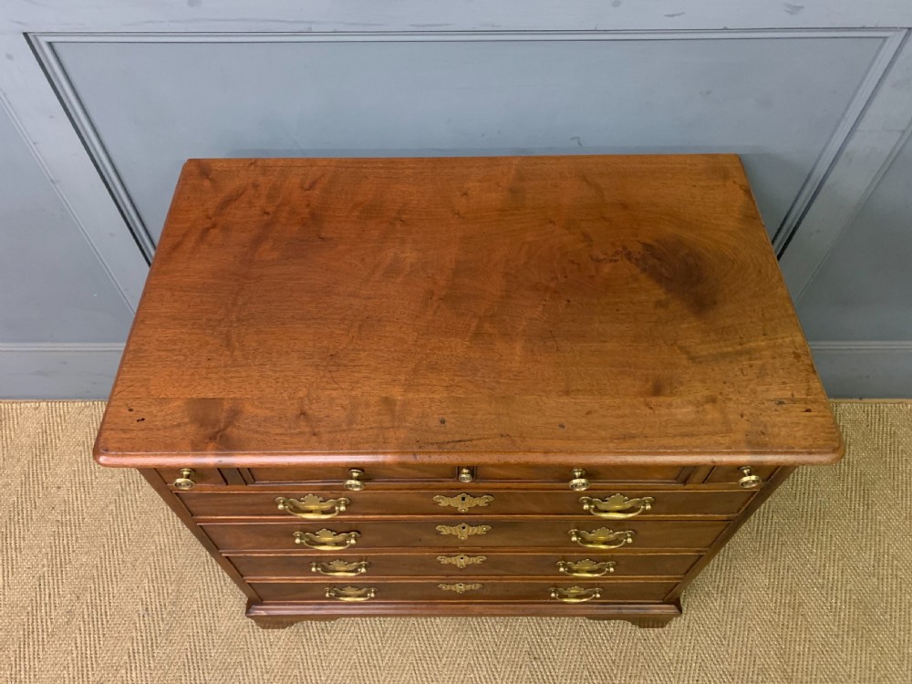 A Georgian mahogany bachelor chest featuring multiple drawers, brass handles, bracket feet, and an extended writing slide lined with green baize. View VI
