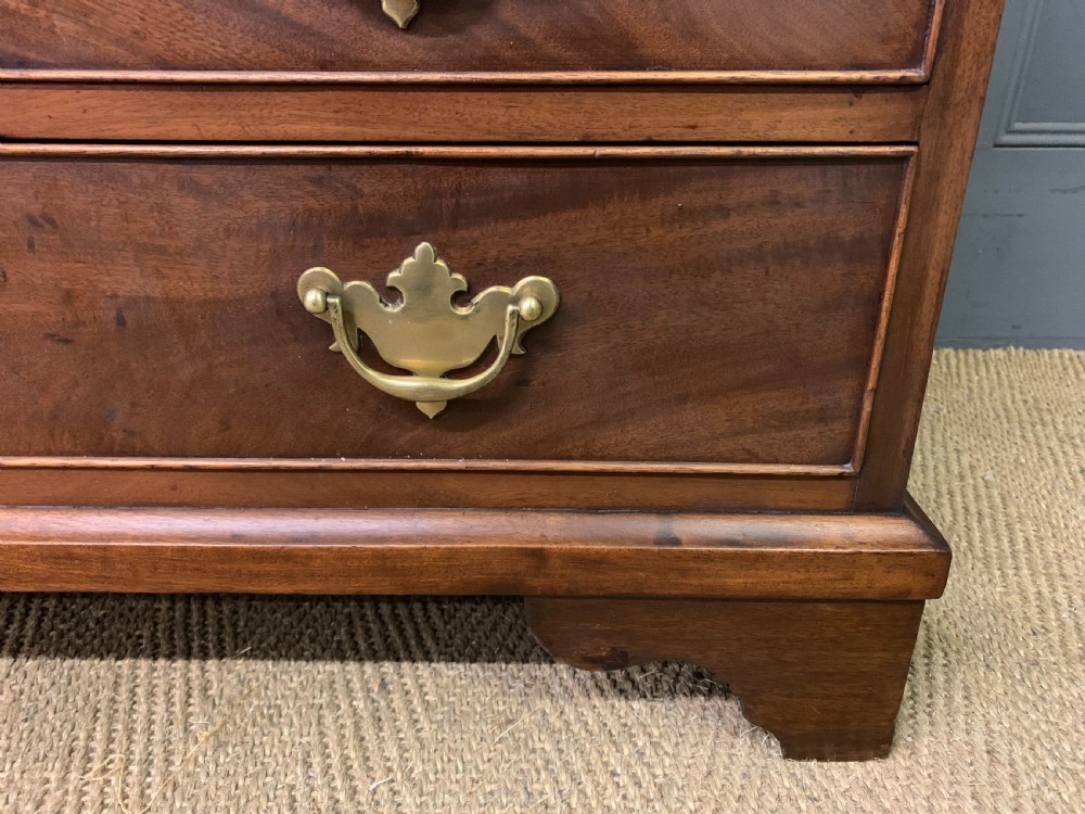 A Georgian mahogany bachelor chest featuring multiple drawers, brass handles, bracket feet, and an extended writing slide lined with green baize. View VIII