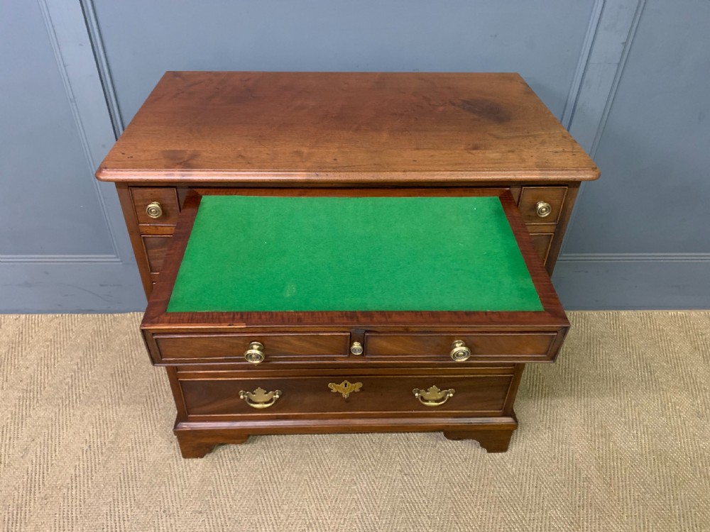 A Georgian mahogany bachelor chest featuring multiple drawers, brass handles, bracket feet, and an extended writing slide lined with green baize. View X