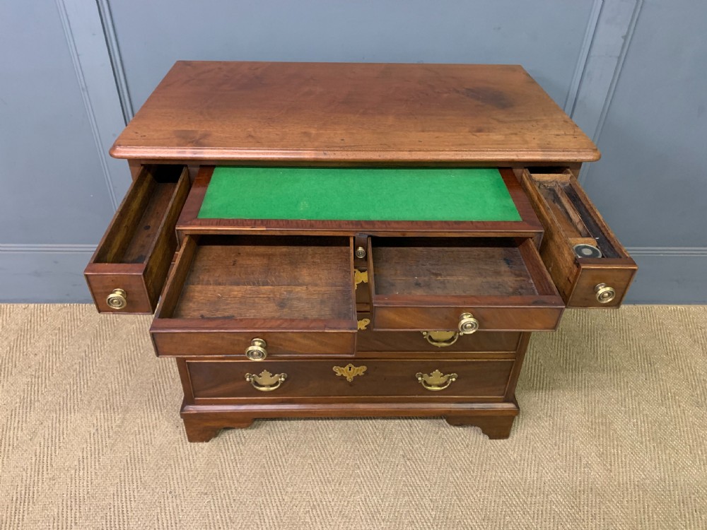A Georgian mahogany bachelor chest featuring multiple drawers, brass handles, bracket feet, and an extended writing slide lined with green baize. View XI