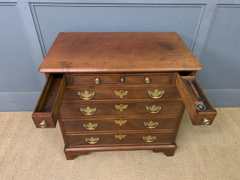 A Georgian mahogany bachelor chest featuring multiple drawers, brass handles, bracket feet, and an extended writing slide lined with green baize. View XIV