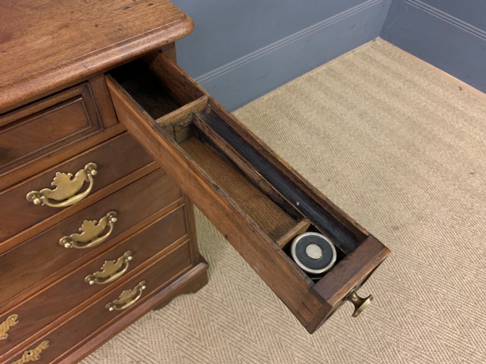 A Georgian mahogany bachelor chest featuring multiple drawers, brass handles, bracket feet, and an extended writing slide lined with green baize. View XV