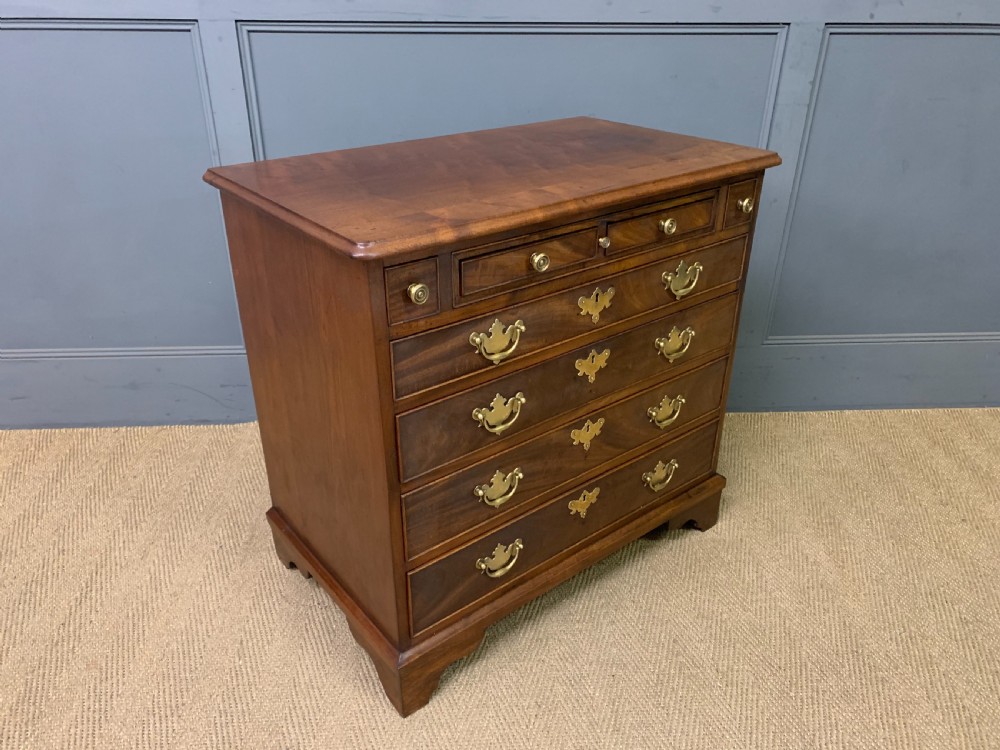 A Georgian mahogany bachelor chest featuring multiple drawers, brass handles, bracket feet, and an extended writing slide lined with green baize. View XVI