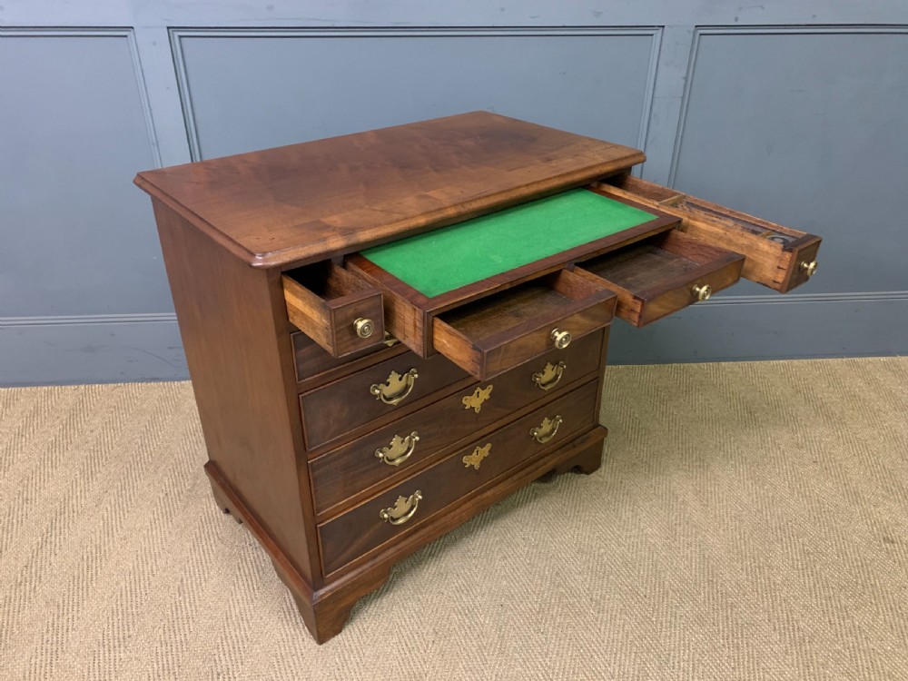 A Georgian mahogany bachelor chest featuring multiple drawers, brass handles, bracket feet, and an extended writing slide lined with green baize. View XIX