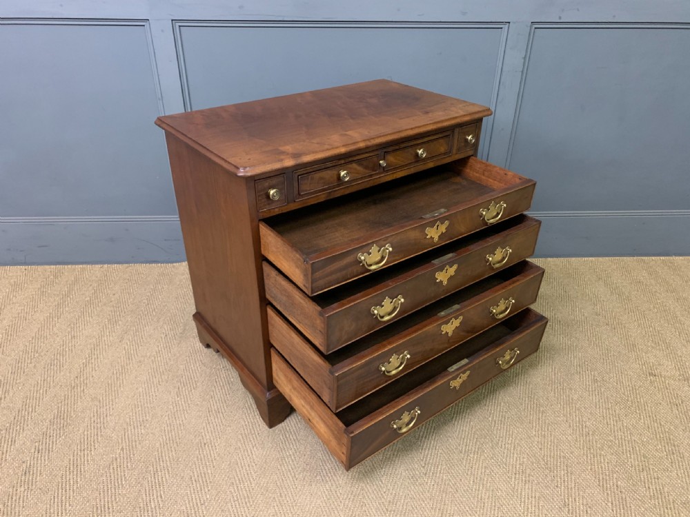 A Georgian mahogany bachelor chest featuring multiple drawers, brass handles, bracket feet, and an extended writing slide lined with green baize. View XX
