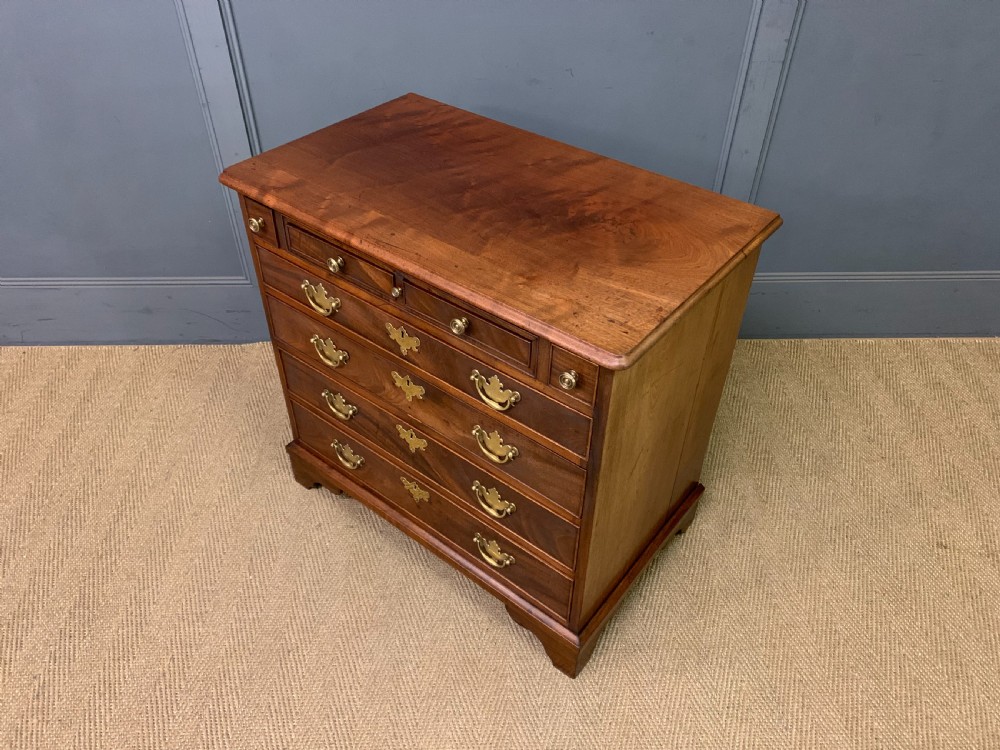A Georgian mahogany bachelor chest featuring multiple drawers, brass handles, bracket feet, and an extended writing slide lined with green baize. View XXI