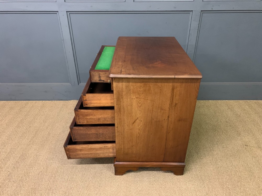 A Georgian mahogany bachelor chest featuring multiple drawers, brass handles, bracket feet, and an extended writing slide lined with green baize. View XXII