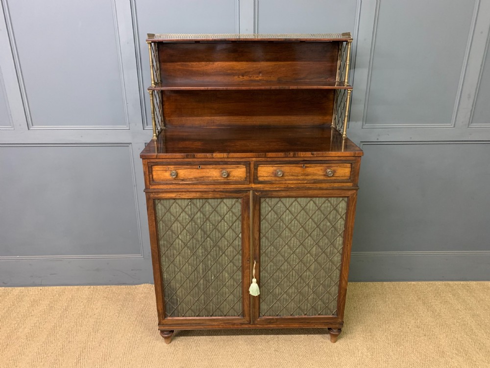 An antique Regency rosewood chiffonier featuring a brass lattice gallery shelf, two upper drawers, and lower doors with wire mesh and pleated fabric panels. View II