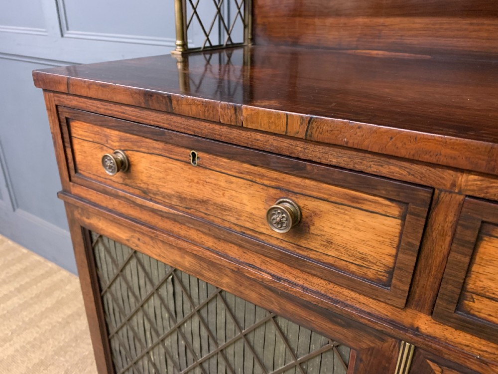 An antique Regency rosewood chiffonier featuring a brass lattice gallery shelf, two upper drawers, and lower doors with wire mesh and pleated fabric panels. View VIII