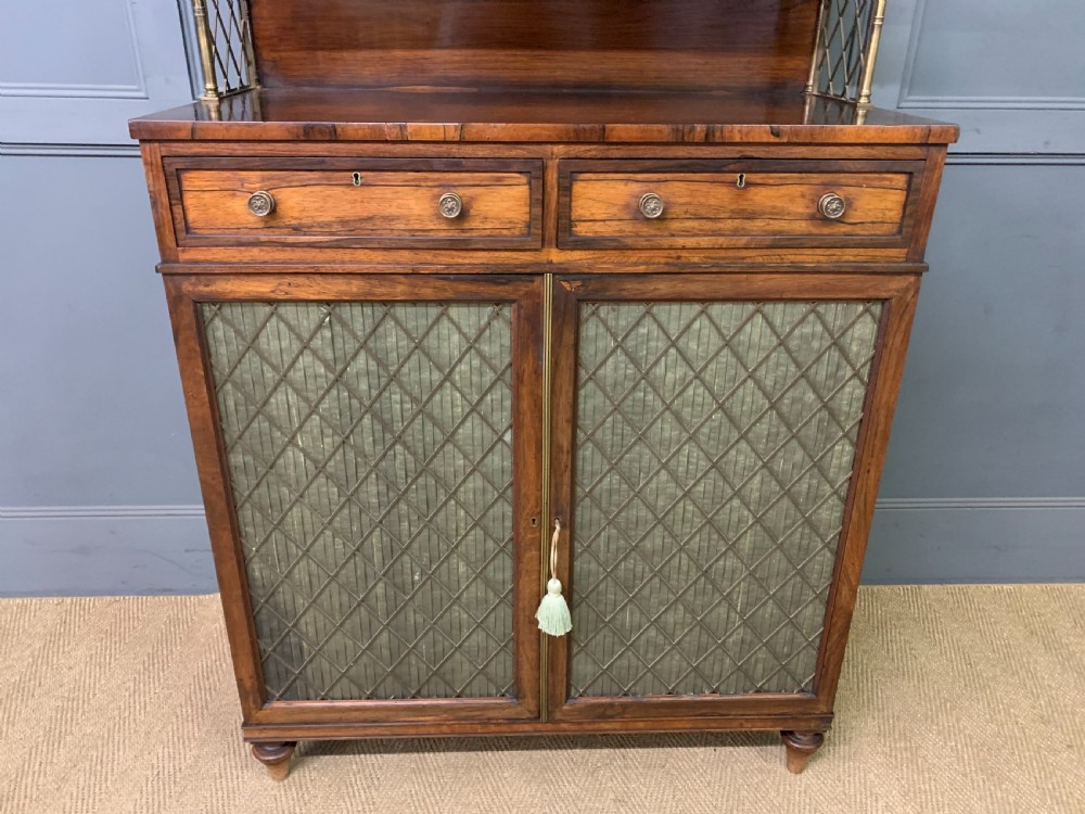 An antique Regency rosewood chiffonier featuring a brass lattice gallery shelf, two upper drawers, and lower doors with wire mesh and pleated fabric panels. View XI