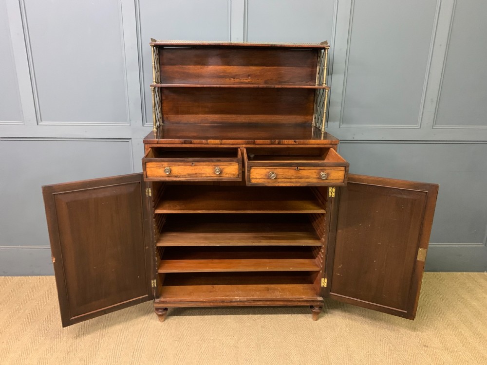 An antique Regency rosewood chiffonier featuring a brass lattice gallery shelf, two upper drawers, and lower doors with wire mesh and pleated fabric panels. View XII
