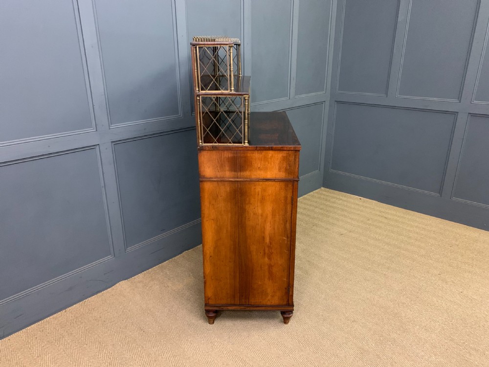 An antique Regency rosewood chiffonier featuring a brass lattice gallery shelf, two upper drawers, and lower doors with wire mesh and pleated fabric panels. View XV