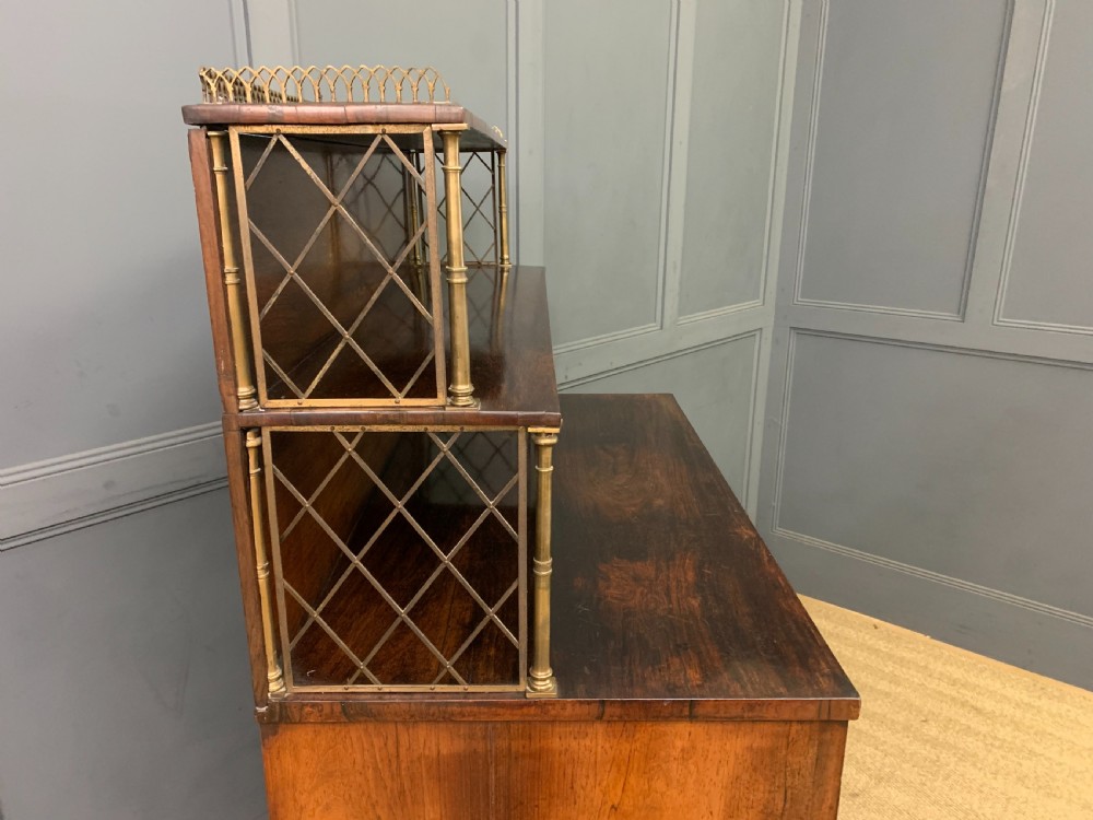 An antique Regency rosewood chiffonier featuring a brass lattice gallery shelf, two upper drawers, and lower doors with wire mesh and pleated fabric panels. View XVI