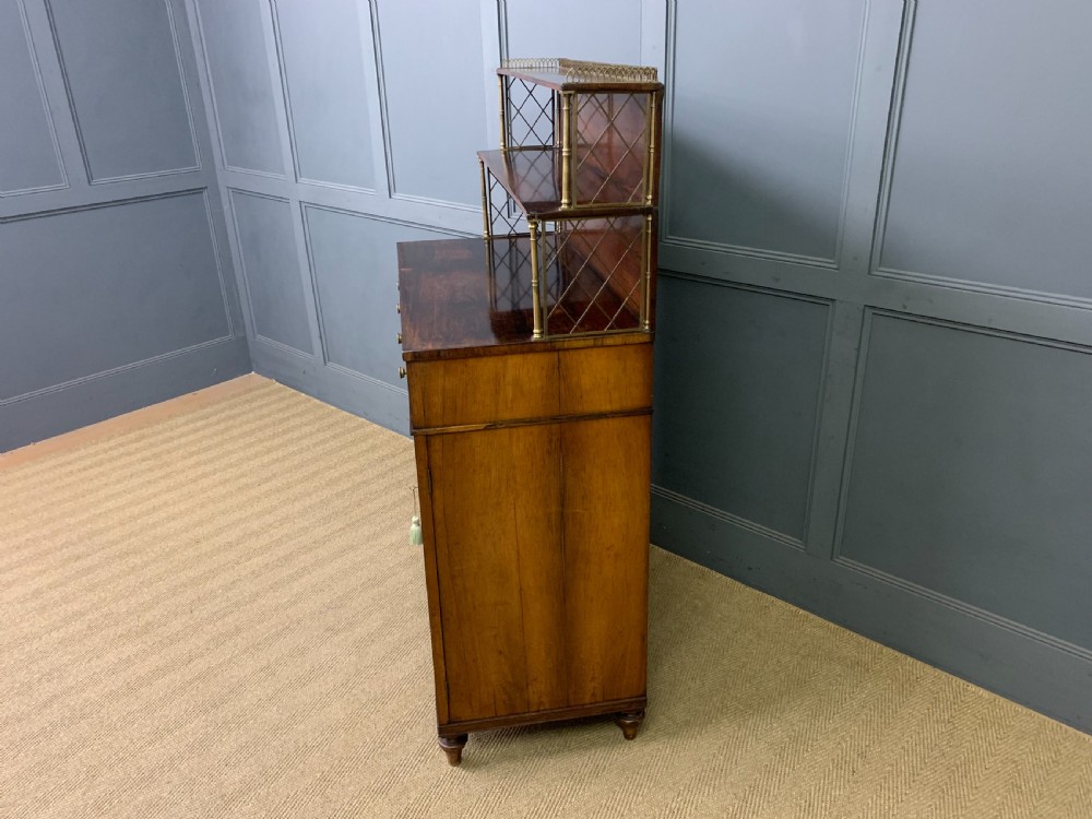 An antique Regency rosewood chiffonier featuring a brass lattice gallery shelf, two upper drawers, and lower doors with wire mesh and pleated fabric panels. View XXI