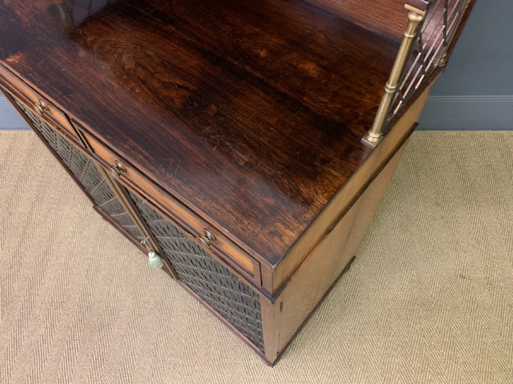 An antique Regency rosewood chiffonier featuring a brass lattice gallery shelf, two upper drawers, and lower doors with wire mesh and pleated fabric panels. View XXII