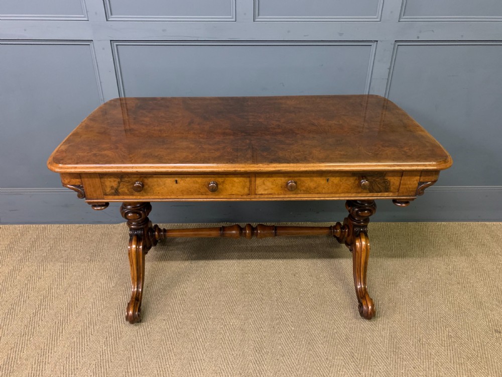 A Victorian burr walnut library table featuring a polished rectangular top with rounded corners, frieze drawers with wooden turned knobs, and twin carved end supports joined by a turned stretcher. View II