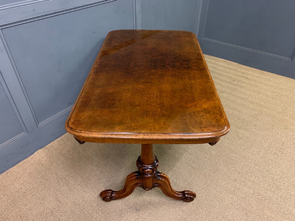 A Victorian burr walnut library table featuring a polished rectangular top with rounded corners, frieze drawers with wooden turned knobs, and twin carved end supports joined by a turned stretcher. View XI