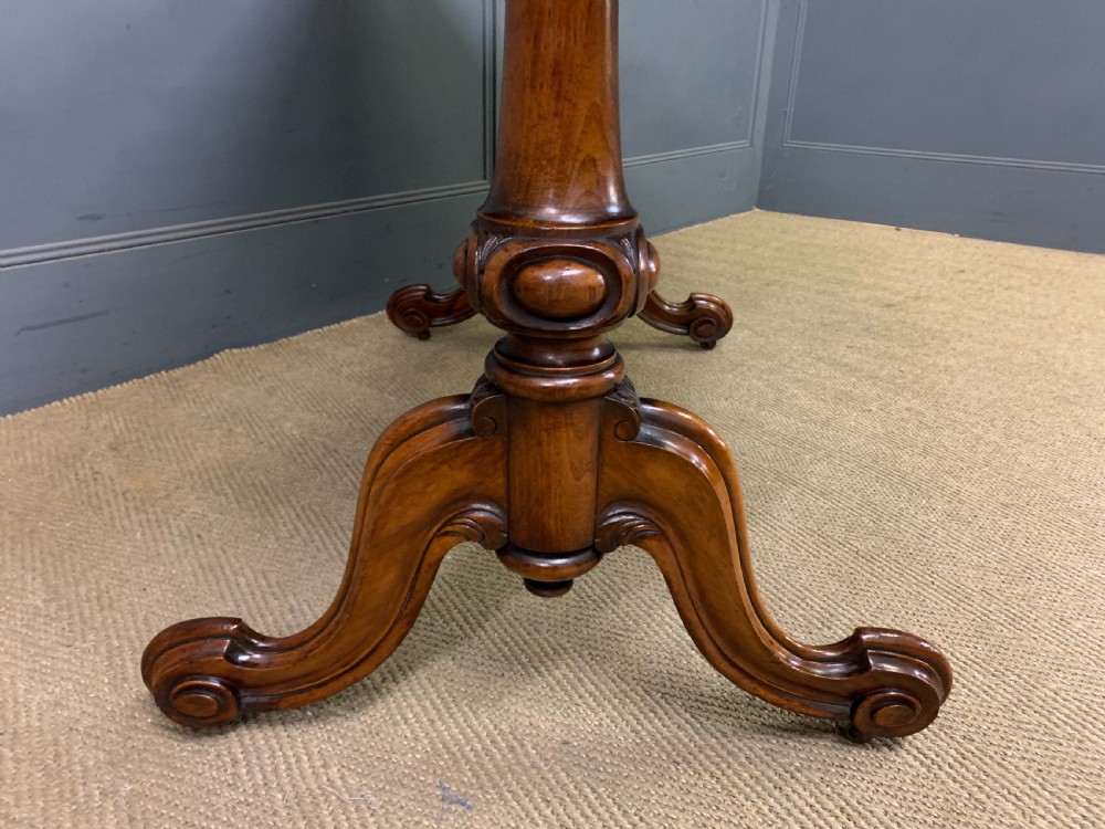 A Victorian burr walnut library table featuring a polished rectangular top with rounded corners, frieze drawers with wooden turned knobs, and twin carved end supports joined by a turned stretcher. View XII