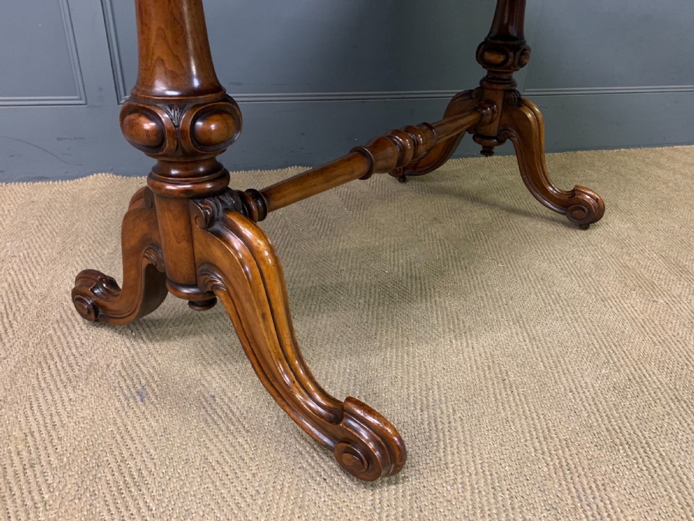 A Victorian burr walnut library table featuring a polished rectangular top with rounded corners, frieze drawers with wooden turned knobs, and twin carved end supports joined by a turned stretcher. View XIII