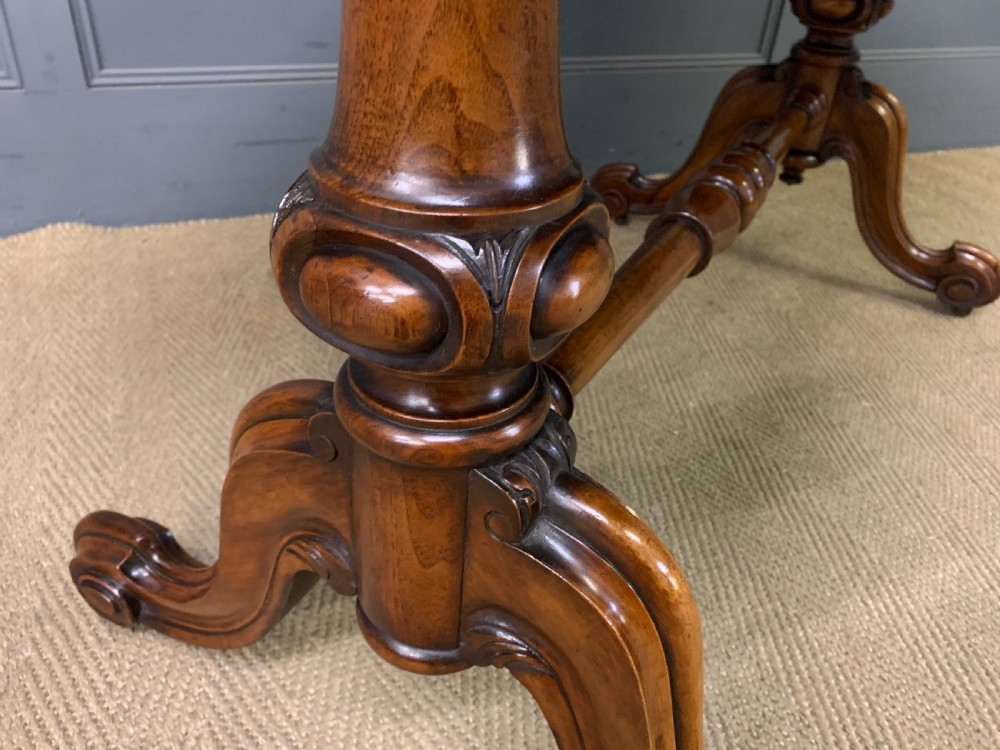 A Victorian burr walnut library table featuring a polished rectangular top with rounded corners, frieze drawers with wooden turned knobs, and twin carved end supports joined by a turned stretcher. View XIV
