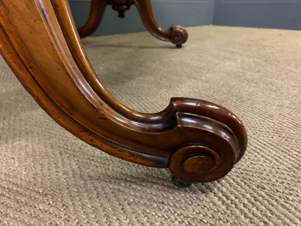 A Victorian burr walnut library table featuring a polished rectangular top with rounded corners, frieze drawers with wooden turned knobs, and twin carved end supports joined by a turned stretcher. View XV