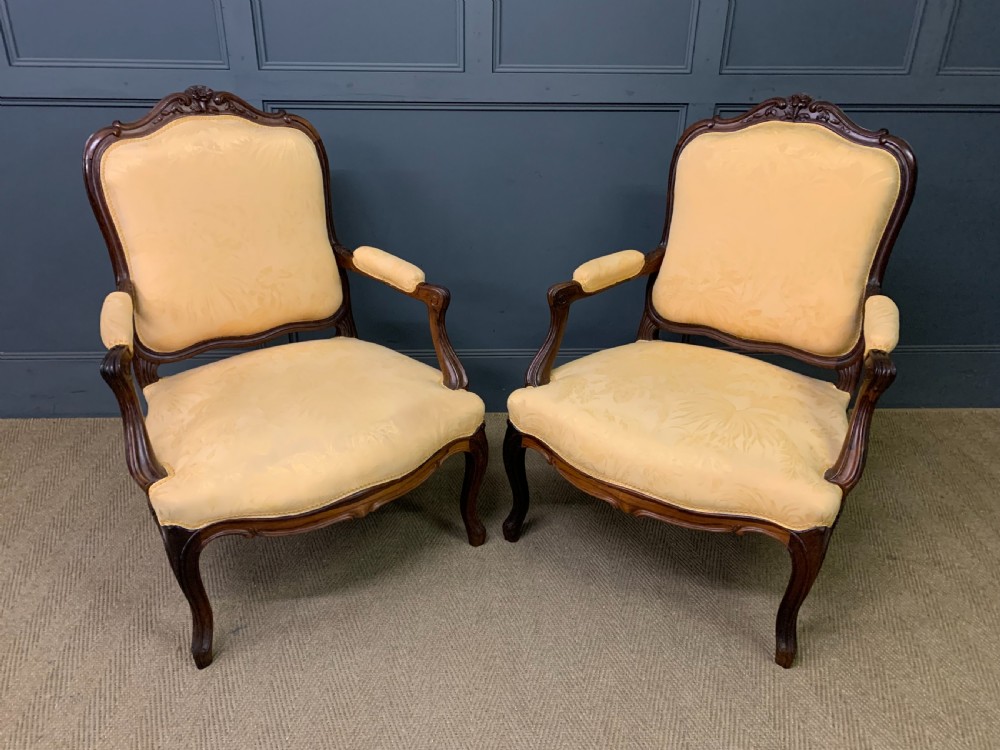 A pair of antique French rosewood fauteuil armchairs with carved serpentine frames, cabriole legs, and yellow floral damask upholstery.