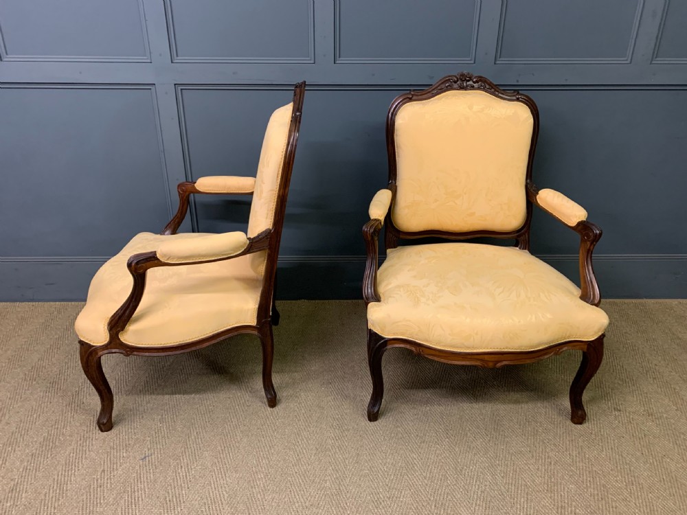 A pair of antique French rosewood fauteuil armchairs with carved serpentine frames, cabriole legs, and yellow floral damask upholstery. View V