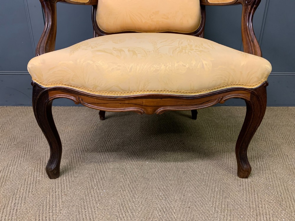 A pair of antique French rosewood fauteuil armchairs with carved serpentine frames, cabriole legs, and yellow floral damask upholstery. View IX