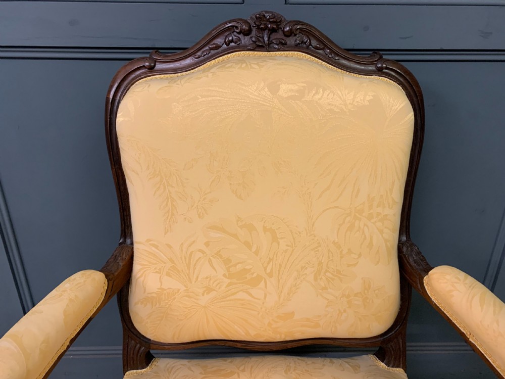 A pair of antique French rosewood fauteuil armchairs with carved serpentine frames, cabriole legs, and yellow floral damask upholstery. View X