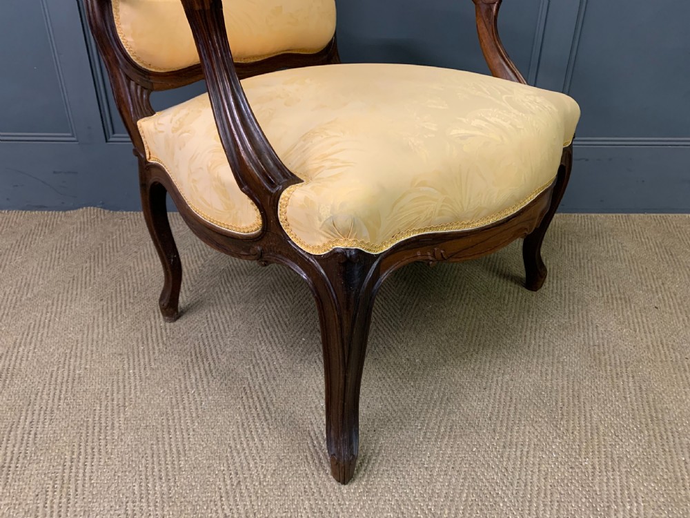 A pair of antique French rosewood fauteuil armchairs with carved serpentine frames, cabriole legs, and yellow floral damask upholstery. View XVII
