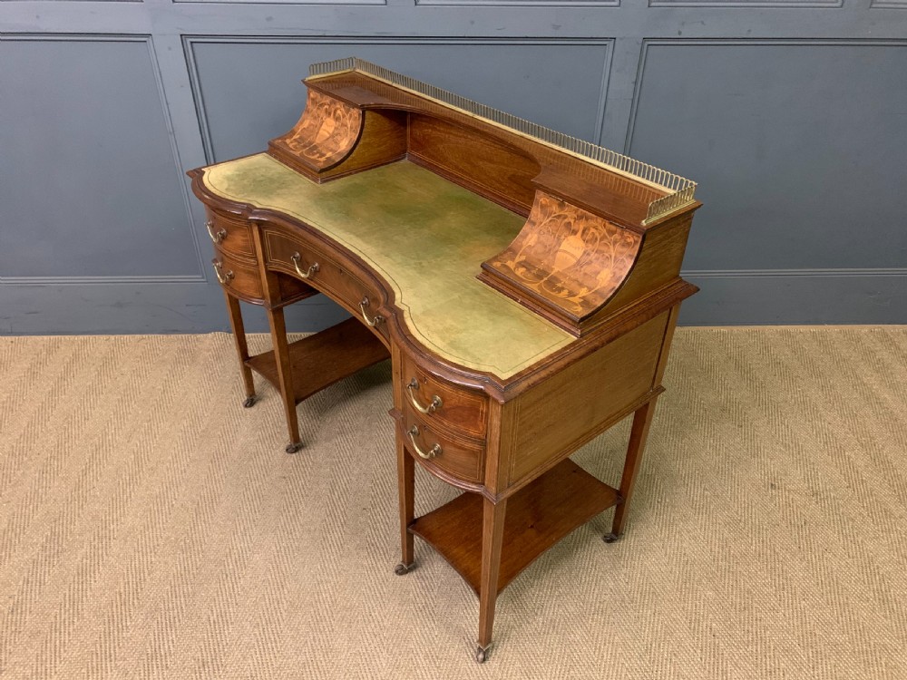 An Edwardian mahogany writing desk featuring a green leather surface, brass gallery rail, marquetry sloped panels, and drawer pedestals on tapered legs.
