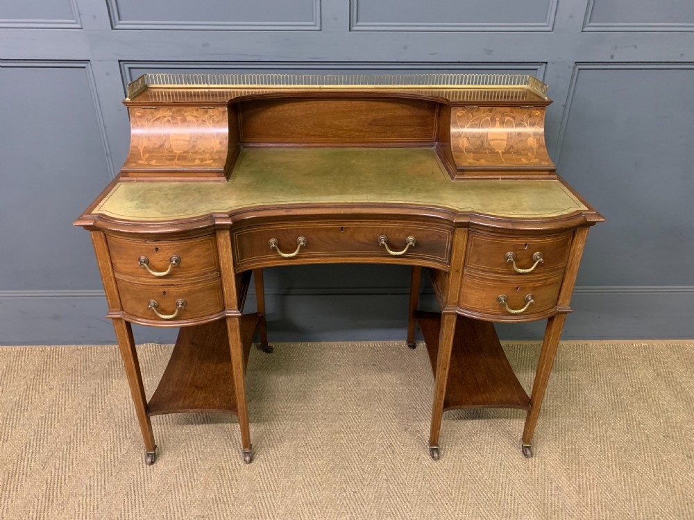 An Edwardian mahogany writing desk featuring a green leather surface, brass gallery rail, marquetry sloped panels, and drawer pedestals on tapered legs. View II