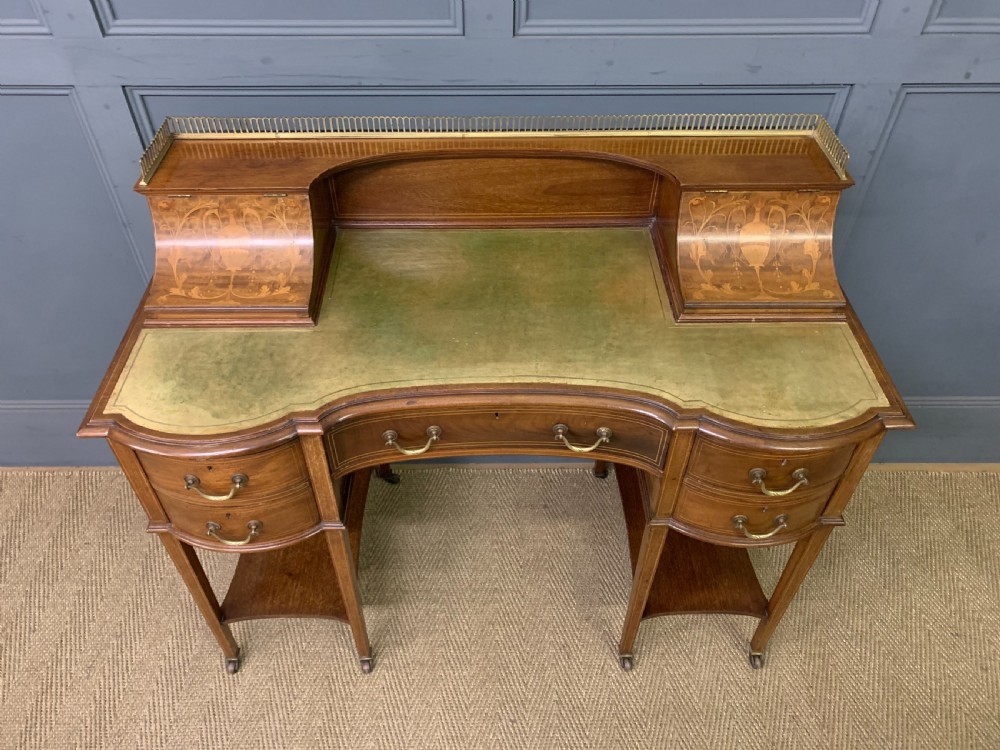 An Edwardian mahogany writing desk featuring a green leather surface, brass gallery rail, marquetry sloped panels, and drawer pedestals on tapered legs. View V