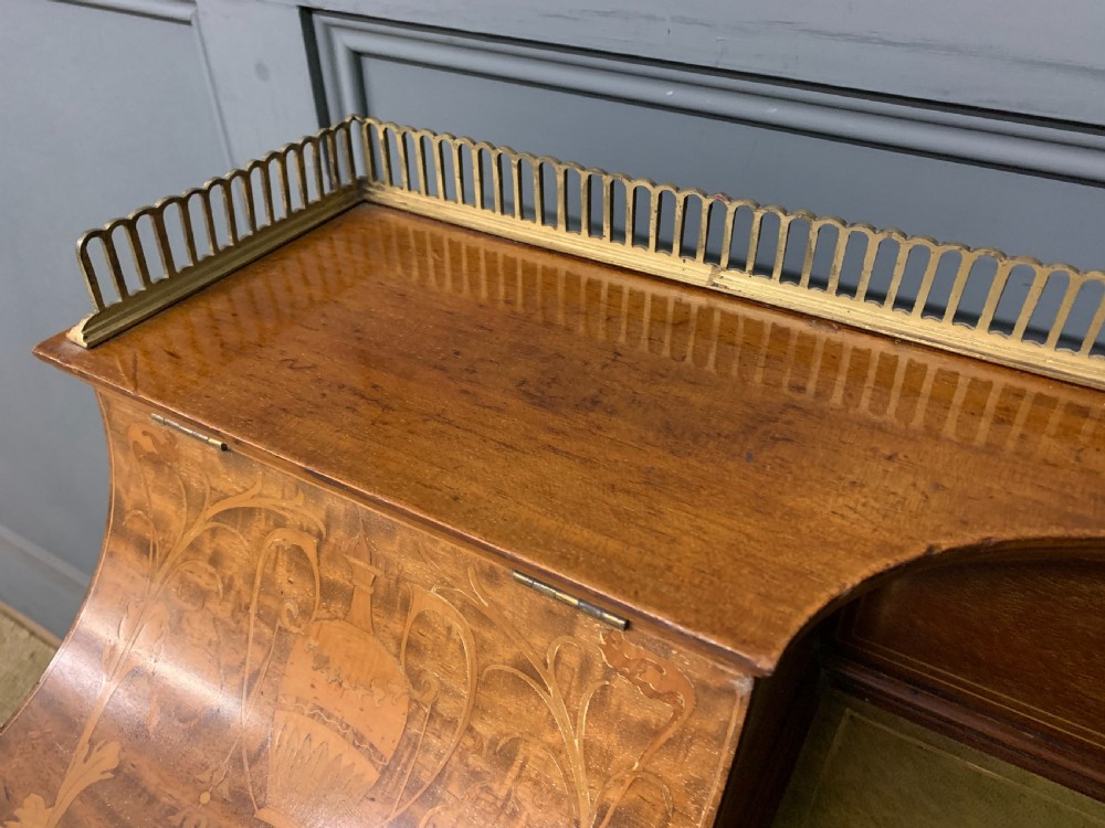 An Edwardian mahogany writing desk featuring a green leather surface, brass gallery rail, marquetry sloped panels, and drawer pedestals on tapered legs. View VI