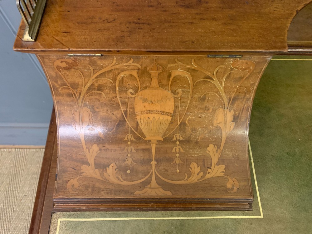 An Edwardian mahogany writing desk featuring a green leather surface, brass gallery rail, marquetry sloped panels, and drawer pedestals on tapered legs. View VII