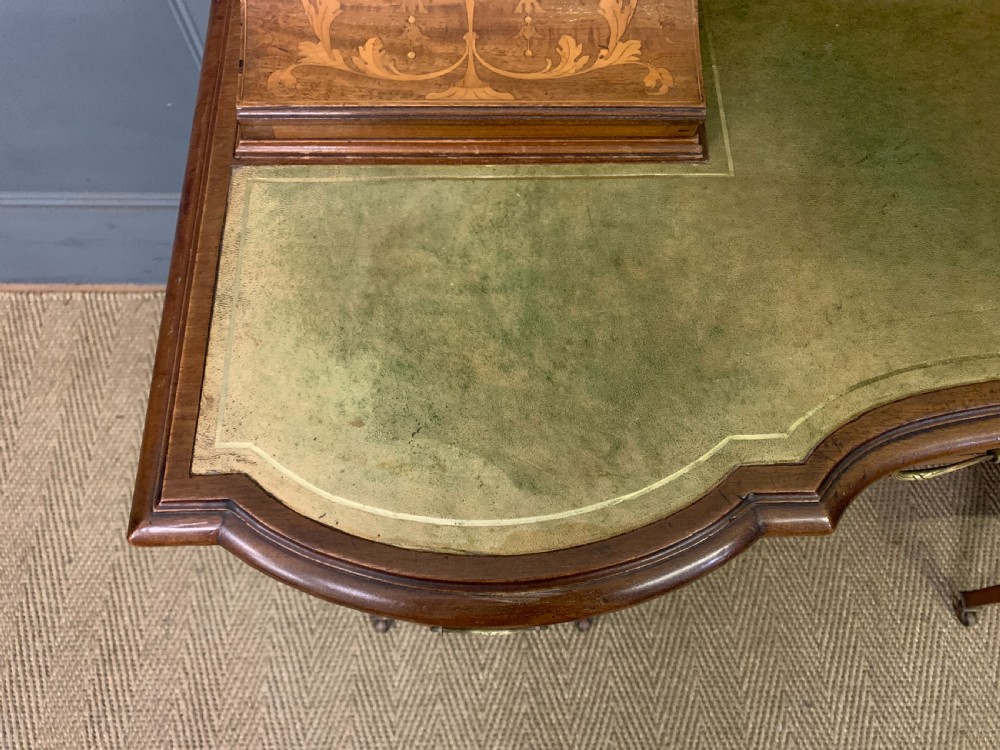An Edwardian mahogany writing desk featuring a green leather surface, brass gallery rail, marquetry sloped panels, and drawer pedestals on tapered legs. View VIII