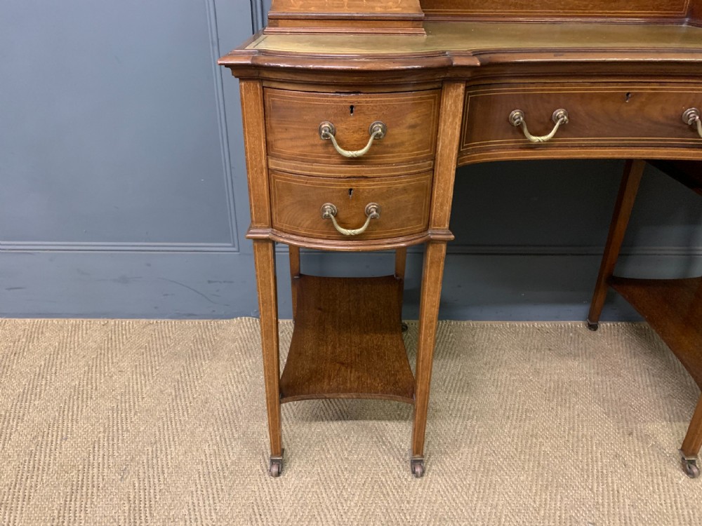 An Edwardian mahogany writing desk featuring a green leather surface, brass gallery rail, marquetry sloped panels, and drawer pedestals on tapered legs. View IX