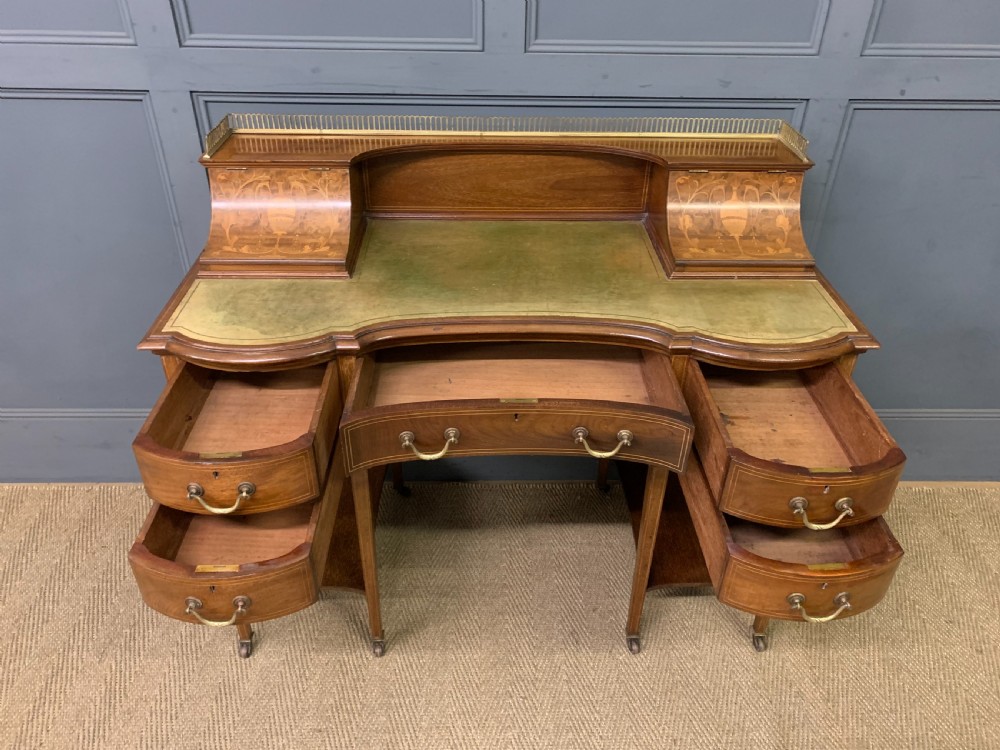 An Edwardian mahogany writing desk featuring a green leather surface, brass gallery rail, marquetry sloped panels, and drawer pedestals on tapered legs. View XII
