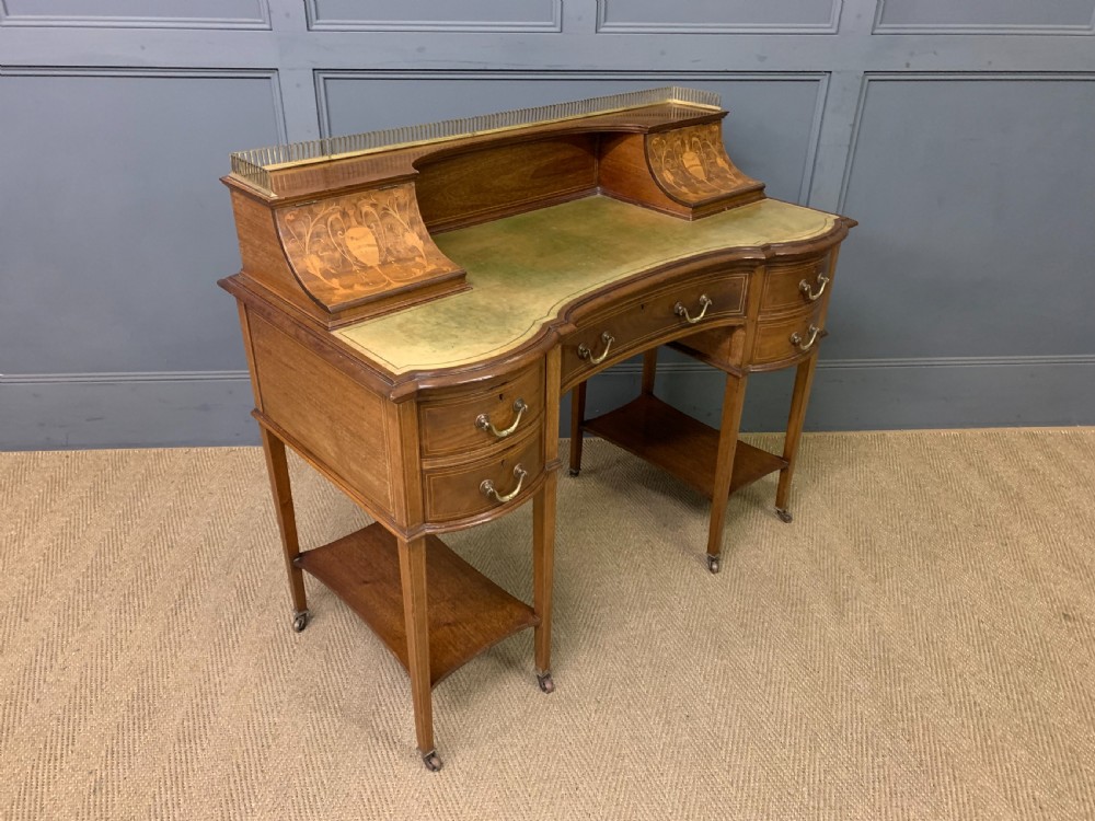 An Edwardian mahogany writing desk featuring a green leather surface, brass gallery rail, marquetry sloped panels, and drawer pedestals on tapered legs. View XV