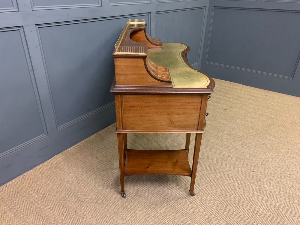 An Edwardian mahogany writing desk featuring a green leather surface, brass gallery rail, marquetry sloped panels, and drawer pedestals on tapered legs. View XVI