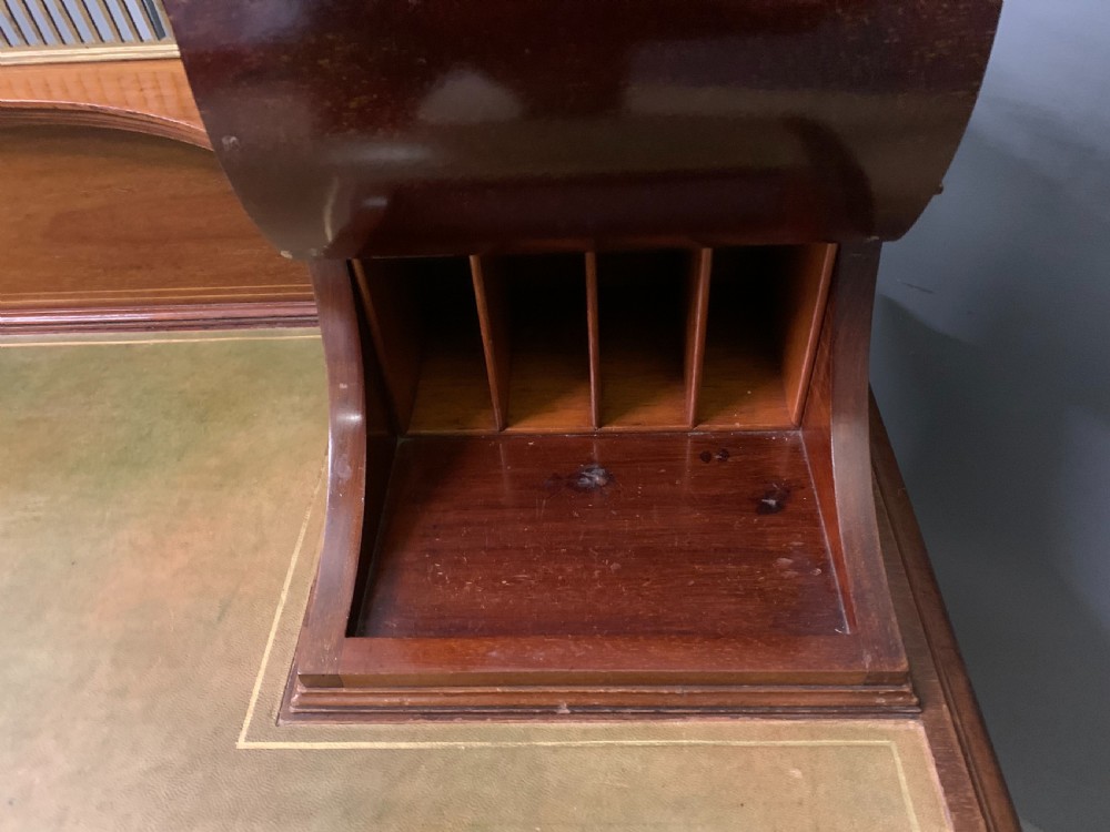 An Edwardian mahogany writing desk featuring a green leather surface, brass gallery rail, marquetry sloped panels, and drawer pedestals on tapered legs. View XIX