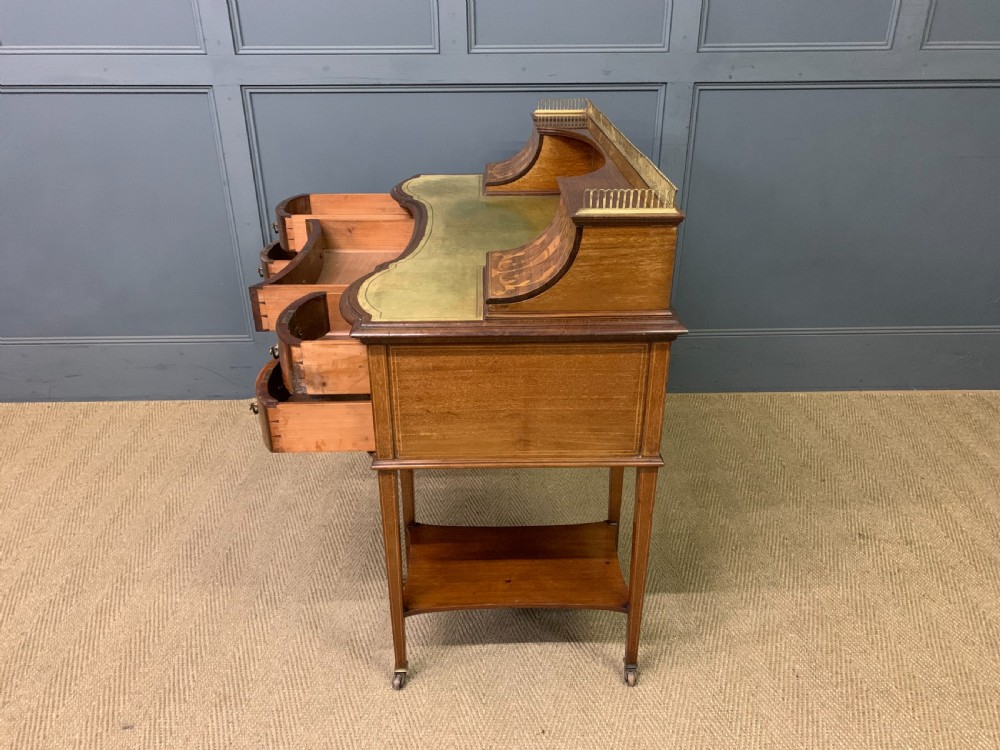 An Edwardian mahogany writing desk featuring a green leather surface, brass gallery rail, marquetry sloped panels, and drawer pedestals on tapered legs. View XX