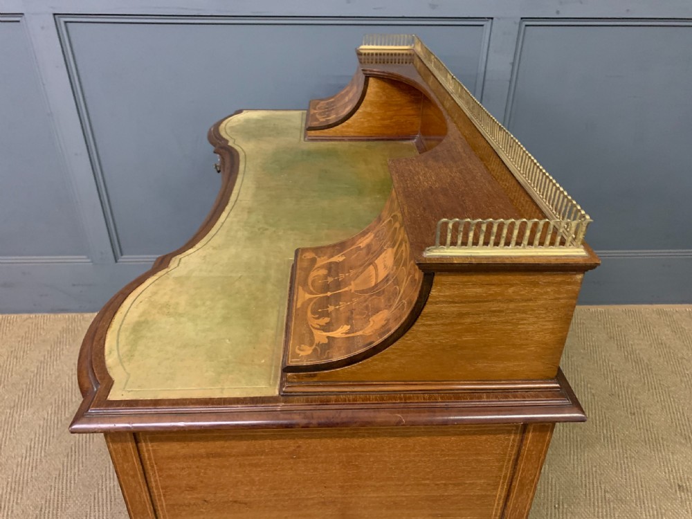 An Edwardian mahogany writing desk featuring a green leather surface, brass gallery rail, marquetry sloped panels, and drawer pedestals on tapered legs. View XXI