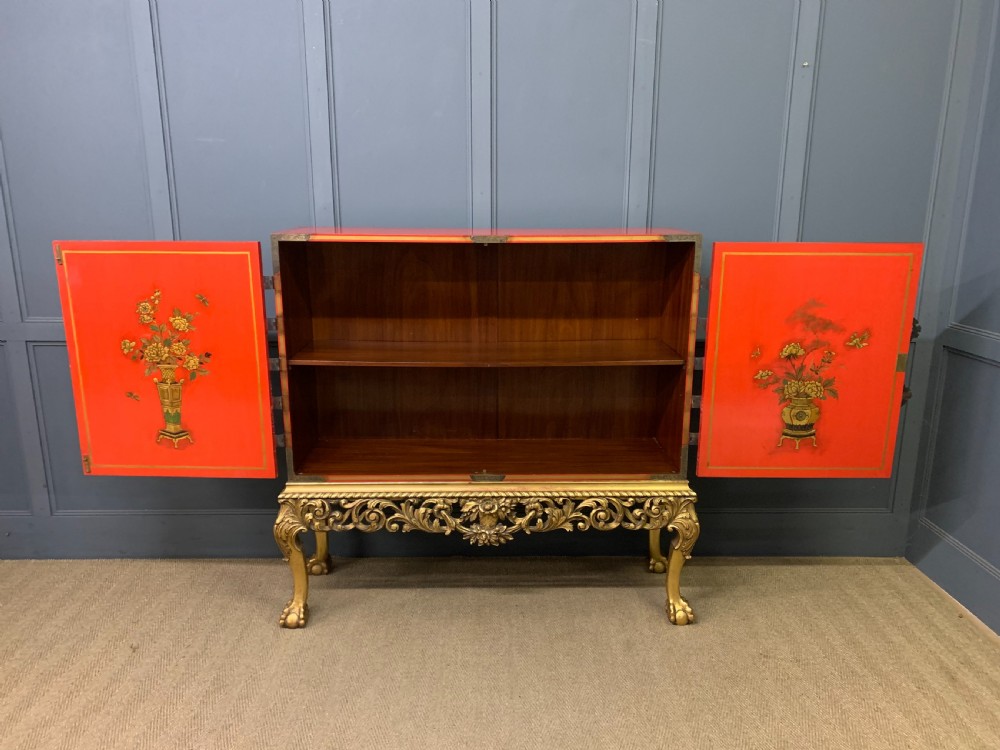 A bright red lacquered Chinoiserie cabinet with gold hand-painted figures and landscapes, mounted on an ornate carved giltwood stand with cabriole legs. View XIV