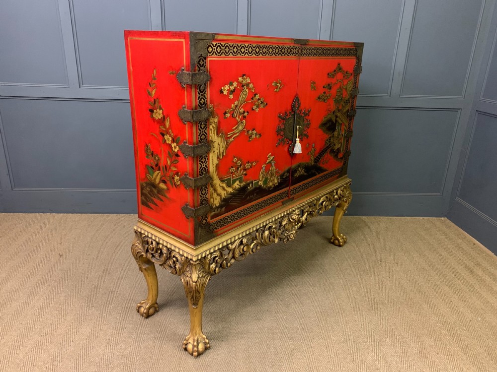 A bright red lacquered Chinoiserie cabinet with gold hand-painted figures and landscapes, mounted on an ornate carved giltwood stand with cabriole legs. View XVII