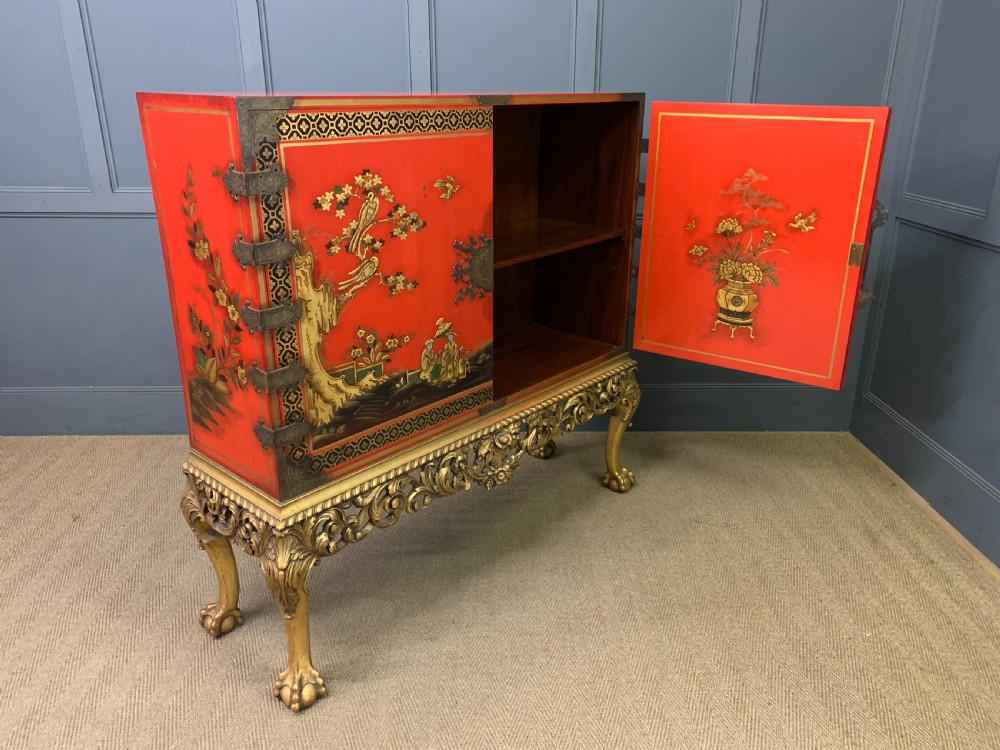 A bright red lacquered Chinoiserie cabinet with gold hand-painted figures and landscapes, mounted on an ornate carved giltwood stand with cabriole legs. View XXI