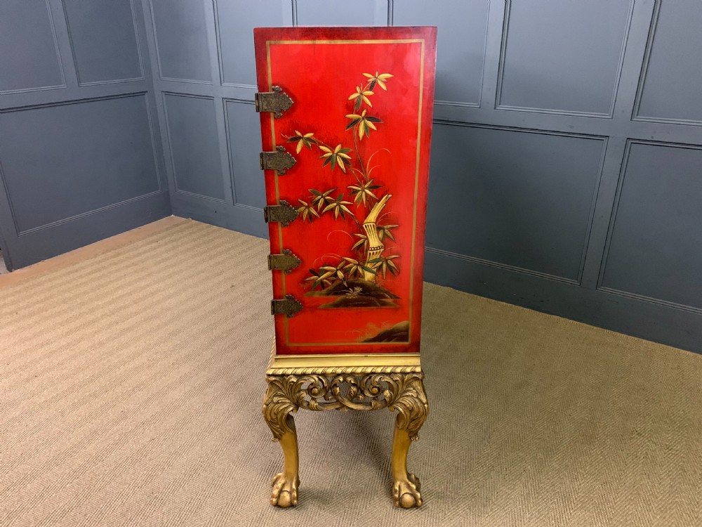 A bright red lacquered Chinoiserie cabinet with gold hand-painted figures and landscapes, mounted on an ornate carved giltwood stand with cabriole legs. View XXII