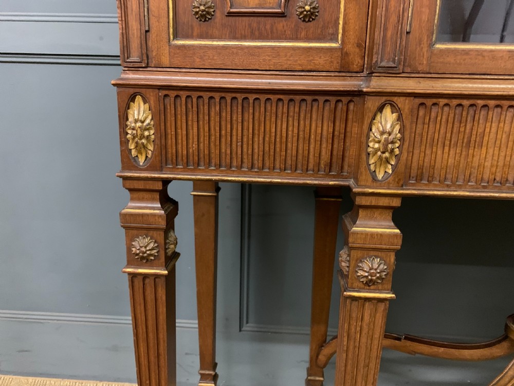 An antique mahogany display cabinet featuring glazed centre doors, side inlaid panels, fluted legs, and an arched top. View VI