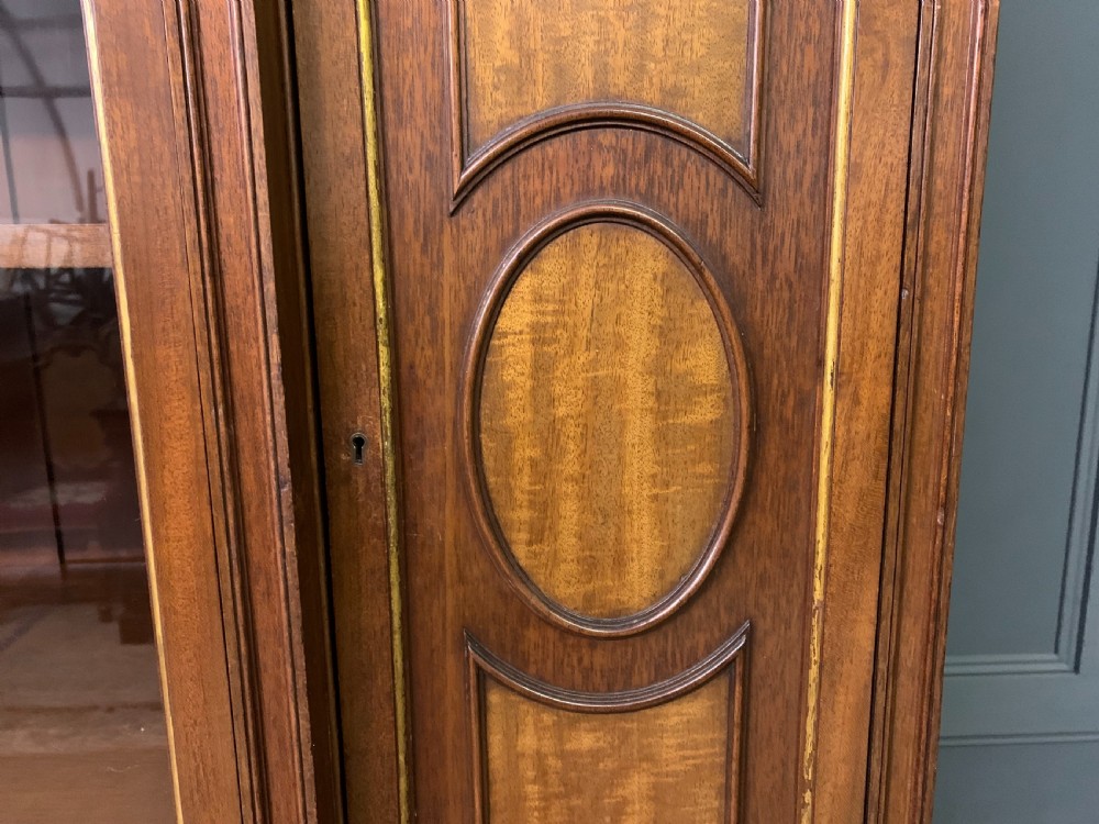 An antique mahogany display cabinet featuring glazed centre doors, side inlaid panels, fluted legs, and an arched top. View XI