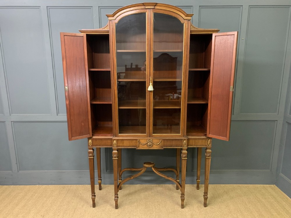 An antique mahogany display cabinet featuring glazed centre doors, side inlaid panels, fluted legs, and an arched top. View XVI